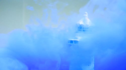 slow motion and close up of a lighthouse underwater with blue water ink swirling around it