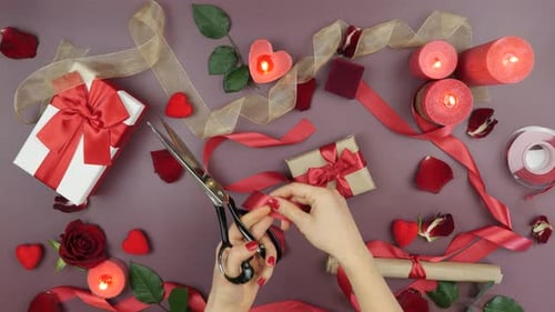 Female hands are cutting red ribbon with scissor on festive St. Valentine's Day background