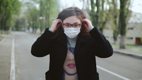 A Young Redhaired Girl Stands on the Street Puts on a Medical Mask