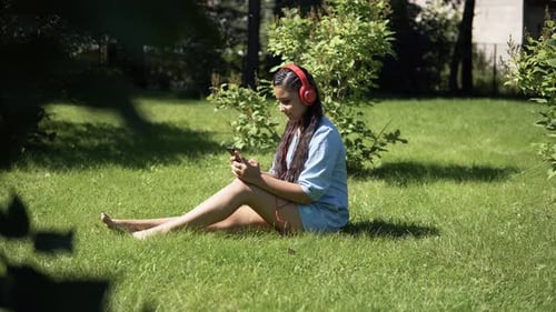Girl Listening to Music on Headphones Sitting on Grass in Park