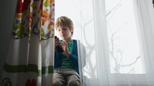 Young Boy on Smartphone by Window Curtains