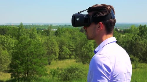 Young Handsome Man Uses Virtual Reality Glasses - Countryside in the Background - Closeup