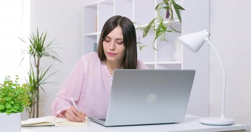 Young Woman Works on Laptop and Writes