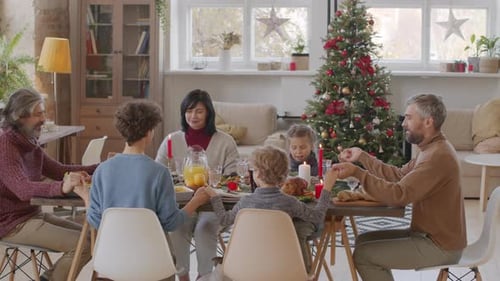Family Holding Hands at Christmas Dinner Table