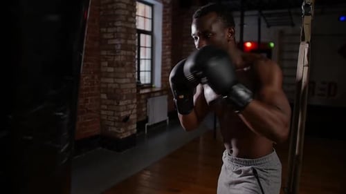 Africanamerican Athletic Shirtless Young Man Boxer Training Punching on the Punching Bag with an