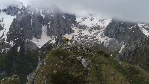 A Hiker Stands on Top of a Mountain and Looks at Snow-capped Mountains, Raising His Hands in Victory