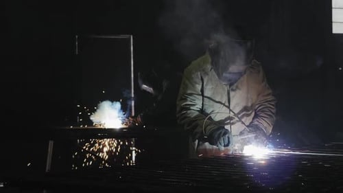 Two Welders Working with Sparks in Dark Factory