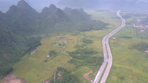 Long Asphalt Road Crosses Valley with Fields and Village