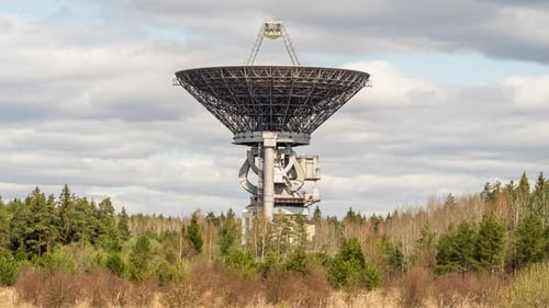 Ein Radioteleskop über dem Wald vor bewölktem Himmel