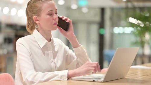 Woman Working at Computer Answers Phone in Office