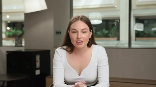 Woman office worker talking on zoom with colleagues at work (look at the camera)