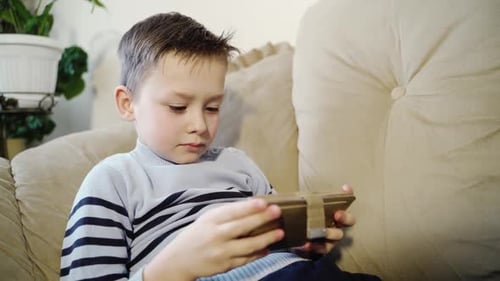 Boy Plays on Tablet Device While Sitting on Couch