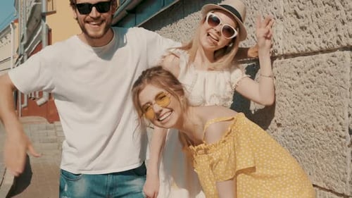 Group of young three stylish friends posing in the street. Fashion man and two cute girls outdoors