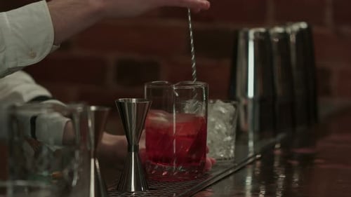 Professional Bartender at Work in Bar Mixing Ice and Liquor in Glass for Drink