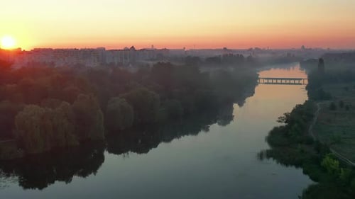 Beautiful red, pink, burgundy, summer sunrise over the river. Fog, bridge, city, trees.
