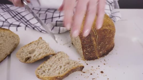 Slicing freshly baked sourdough wheat bread on a white cutting board.