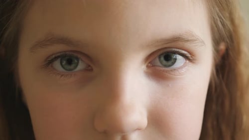 Close Up Blue Eyes of Unhappy Small Blonde Girl Blinking and Looking Into Camera with a Tired Sight