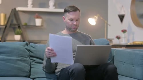 Adult Reviewing Documents While Using Laptop at Home
