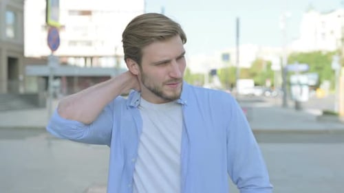 Young Adult Man Rubbing His Neck Outdoors