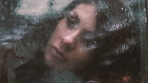 traurige Frau im Auto hinter dem Fenster eingesperrt, nass von Regen, verloren in ihren Gedanken
