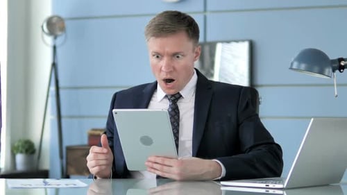 Man Shocked by Results on Tablet at Office Desk