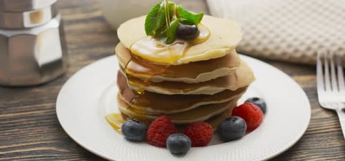 Essens- und Kochkonzept. Stapel Pfannkuchen mit Beeren und warmem Ahornsirup in Zeitlupe