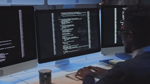 Young Adult Coding at Desk With Three Monitors