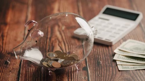 A Hand Inserting Coins in Piggybank Over Wooden Desk