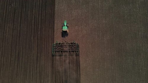 Tractor with harrow system plowing ground on cultivated farm field, agriculture.