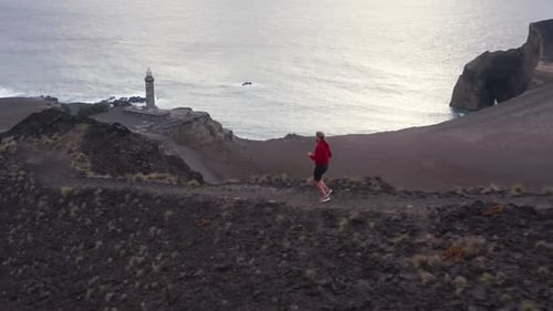 Jogger läuft auf einem Fußweg mit dem Vulkan Capelinhos im Hintergrund der Insel Faial