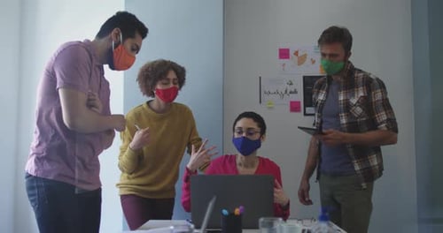 Diverse colleagues wearing face masks working together in meeting room at modern office