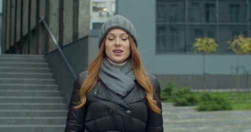 Portrait Shot of Beautiful Young Redhead Woman in a Hat Walking on the Street and Looking at Camera