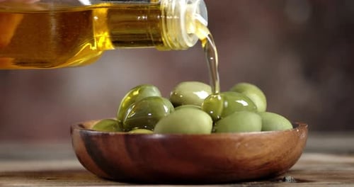 Olive Oil Being Poured Over Green Olives in Bowl
