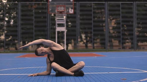 Young Man Stretching on Basketball Court Outdoors