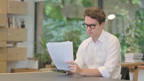 Young Man Reading Documents While Sitting in Modern Office
