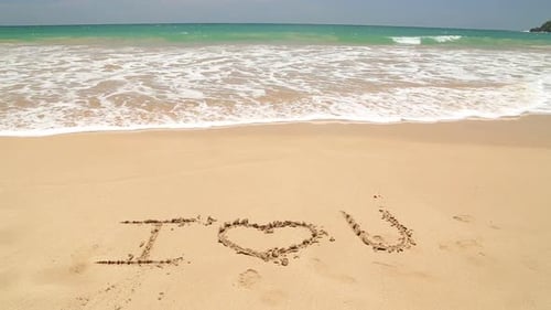 I LOVE U geschrieben im Strandsand, der von Wellen weggespült wird.