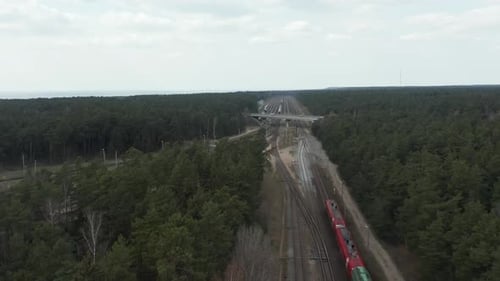 LUFTAUFNAHME: Roter und grüner Güterzug, der auf einer Eisenbahn unter einer Brücke fährt
