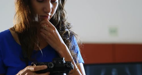 Young Woman Adjusting Digital Camera Indoors