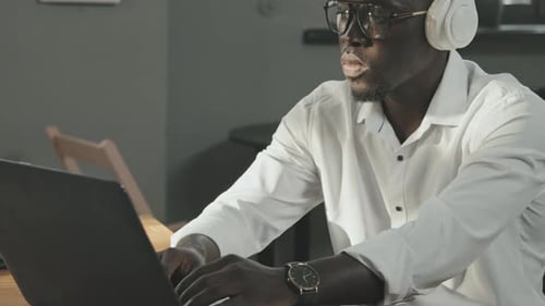 African-American Man in Headphones Typing on Laptop in Office