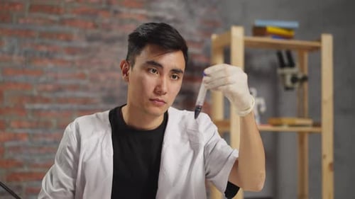 Asian Lab Assistant Shakes Test Tube with Blood in Clinic