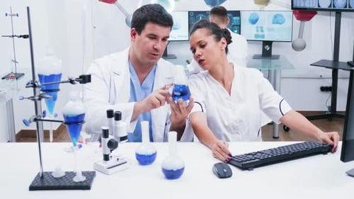 Young Female Scientist in White Coat Working with Her Assistant in a Modern Research Laboratory