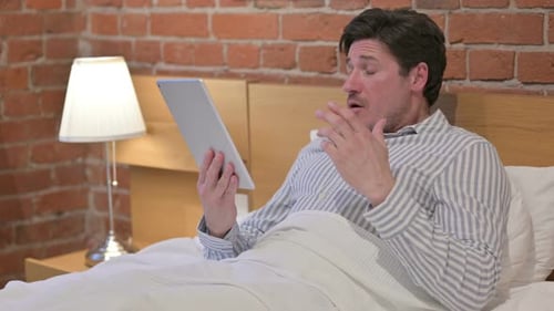 Man Using a Tablet While Lying in Bed