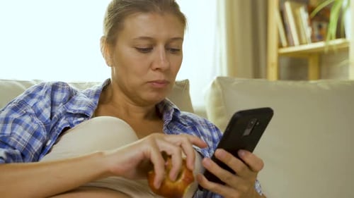Woman Eating an Apple and Using Smartphone Indoors