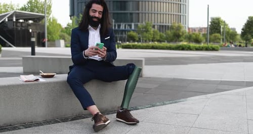 Business man with prosthetic leg using mobile phone outdoor from office building - Job and insurance