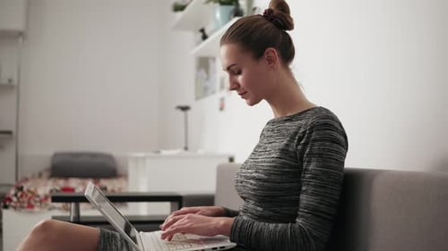 Closeup View of Young Woman at Home Sitting on the Sofa Working with a Laptop and Typing Text Fast