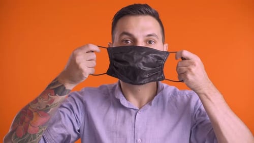 Young Man Putting Black Face Mask and Giving Thumbs Up, Studio Shot