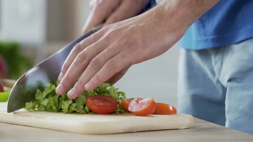 Close-up mail hands cutting tomatoes and lettuce leaves making vegetable salad