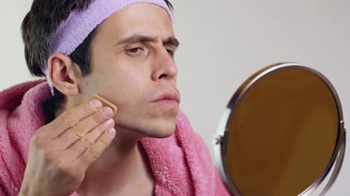 Man Applying Makeup with Sponge Looking at Mirror