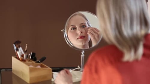 Woman Applying Makeup in Front of Vanity Mirror