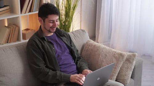 Smiling Man Using Laptop on Couch at Home